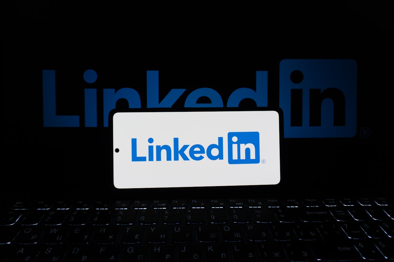 Smartphone showing LinkedIn logo with keyboard and large background logo, business theme.